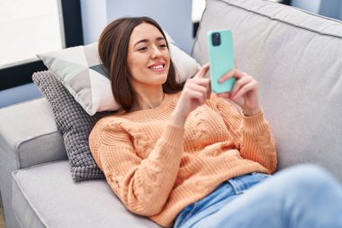 Evdeki kanepede uzanmış akıllı telefon kullanan genç, güzel İspanyol kadın.