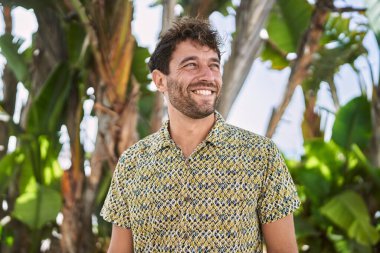 Genç İspanyol adam parkta yürürken kendinden emin gülümsüyor.