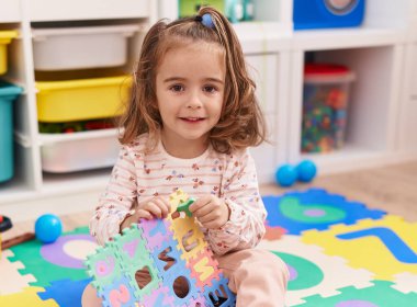 Adorable hispanic girl smiling confident sitting on floor at kindergarten
