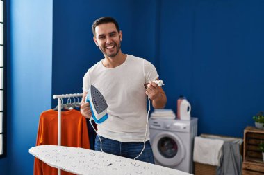 Young hispanic man with beard ironing clothes at home smiling and laughing hard out loud because funny crazy joke. 