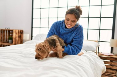 Genç, güzel, İspanyol bir kadın yatakta köpeğe sarılıyor.