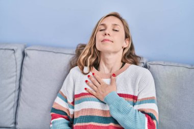 Kanepede oturan genç sarışın kadın evinde kalp krizi geçiriyor.