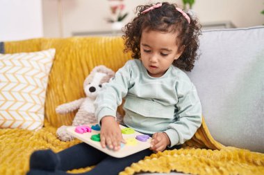 Adorable hispanic girl playing maths game sitting on sofa at home