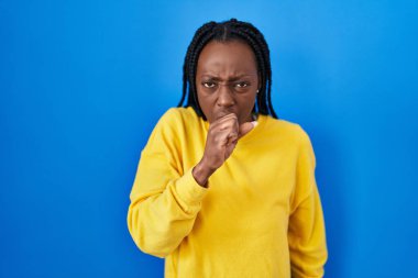 Beautiful black woman standing over blue background feeling unwell and coughing as symptom for cold or bronchitis. health care concept. 