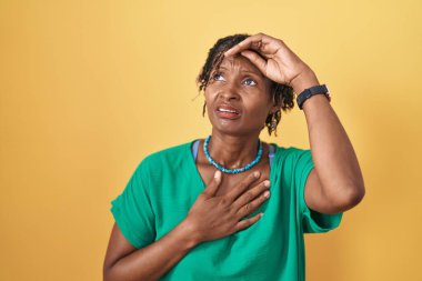 African woman with dreadlocks standing over yellow background touching forehead for illness and fever, flu and cold, virus sick 