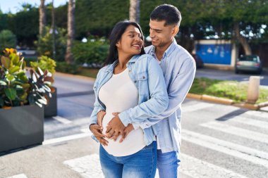 Latin bir çift bebek bekliyor. Sokakta birbirlerine sarılıyorlar.