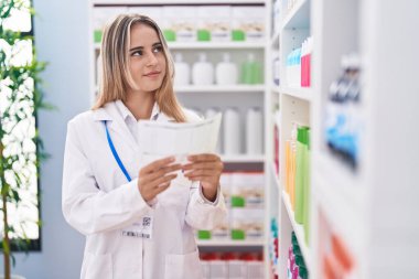 Young blonde woman pharmacist reading prescription at pharmacy
