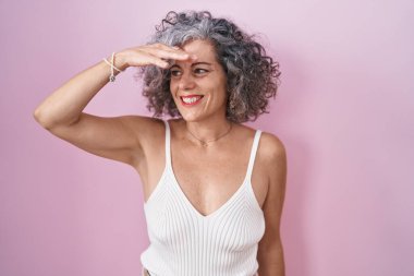 Pembe arka planda gri saçlı orta yaşlı bir kadın. Çok mutlu ve gülümsüyor. Çok uzaklara bakıyor. arama kavramı. 