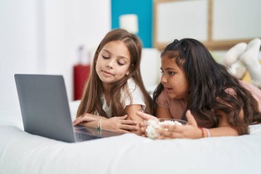Two kids watching movie on laptop lying on bed at bedroom