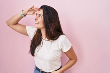 Pembe arka planda duran genç esmer kadın çok mutlu ve gülümsüyor. arama kavramı. 