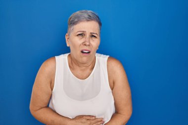 Orta yaşlı, beyaz bir kadın midesi üzerinde el üstünde duruyor çünkü hazımsızlık, acı verici bir hastalık kendini iyi hissetmiyor. Ağrı kavramı. 