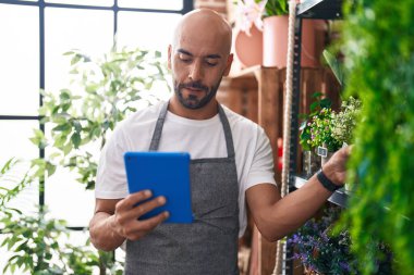 Young bald man florist using touchpad holding plant at florist