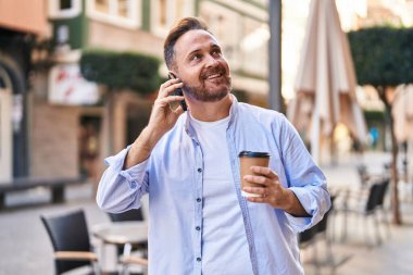 Kafkasyalı genç adam akıllı telefonda konuşuyor kahve dükkanının terasında kahve içiyor.