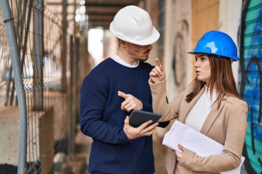 Mand and woman architects using touchpad speaking at street
