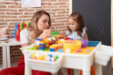 Teacher and toddler playing with construction blocks sitting on table at kindergarten