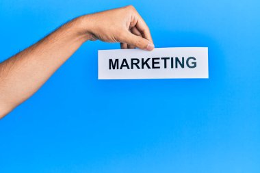 Hand of caucasian man holding paper with marketing word over isolated blue background