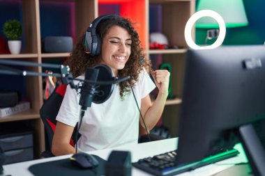 Hispanic woman with curly hair playing video games screaming proud, celebrating victory and success very excited with raised arm 