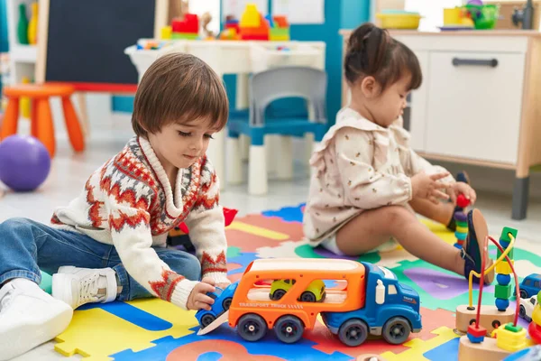 Two kids playing with cars toy sitting on floor at kindergarten