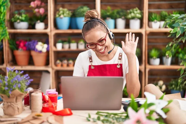 Young hispanic woman working at florist shop doing video call looking positive and happy standing and smiling with a confident smile showing teeth