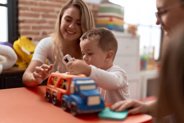 Teachers with boy and girl playing with cars toy sitting on table at kindergarten