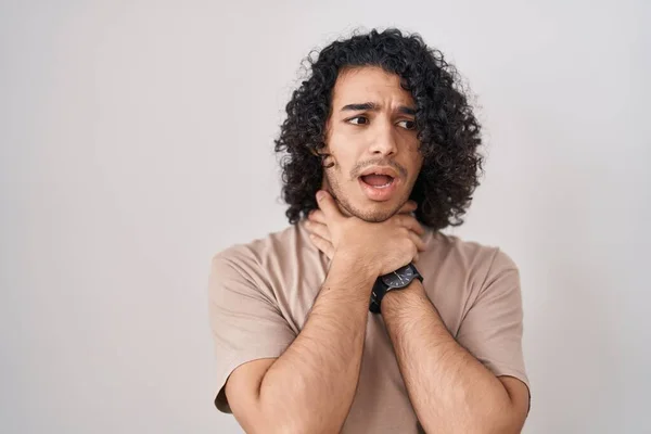 Hispanic man with curly hair standing over white background shouting suffocate because painful strangle. health problem. asphyxiate and suicide concept.