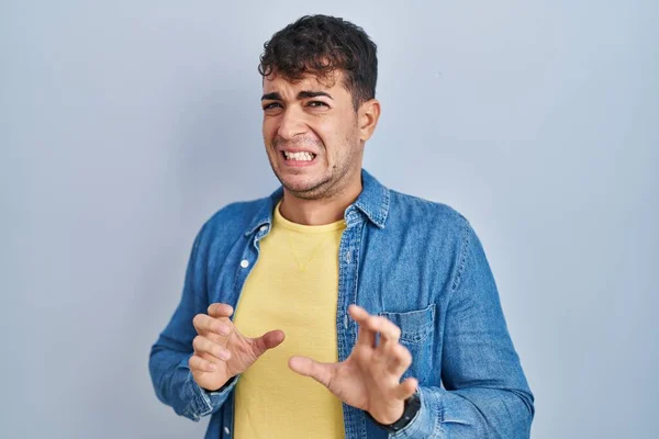 Young hispanic man standing over blue background disgusted expression, displeased and fearful doing disgust face because aversion reaction.