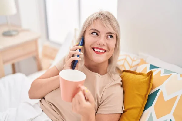 Akıllı Telefondan Konuşan Genç Sarışın Kadın Yatak Odasında Kahve Içiyor — Stok fotoğraf