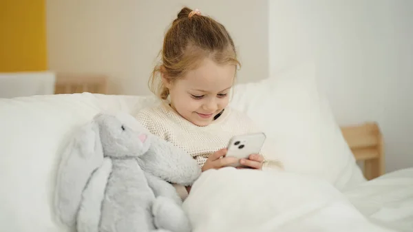 Adorable Blonde Girl Using Smartphone Sitting Bed Bedroom — Stok fotoğraf