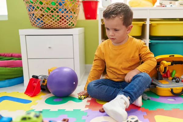 幼稚園の床に座っている車のおもちゃで遊ぶ愛らしい白人少年 — ストック写真