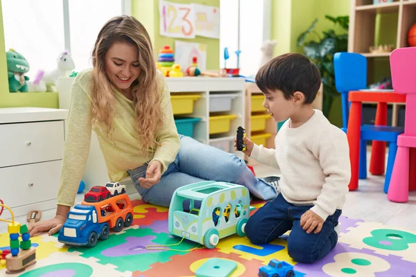 Teacher and toddler playing with cars toy sitting on floor at kindergarten