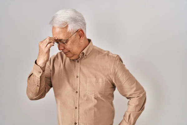 Hispanic senior man wearing glasses tired rubbing nose and eyes feeling fatigue and headache. stress and frustration concept.