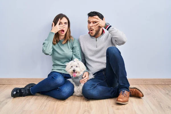 Young Hispanic Couple Sitting Floor Dog Peeking Shock Covering Face — Stockfoto