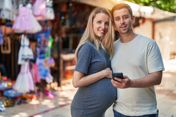 男性と女性のカップルは 路上市場でスマートフォンを使用して赤ちゃんを期待 — ストック写真