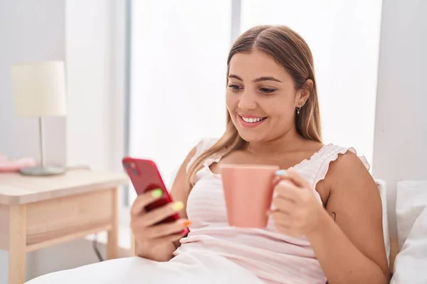 Young Beautiful Hispanic Woman Using Smartphone Drinking Coffee Bedroom — ストック写真