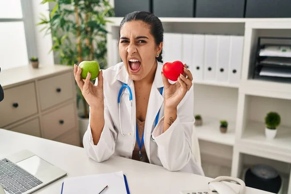 Young Hispanic Woman Working Dietitian Clinic Holding Green Apple Angry — Stockfoto