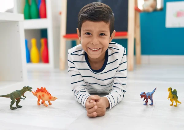 愛らしいHispanic男の子遊びとともにディノおもちゃ嘘で床に幼稚園 — ストック写真