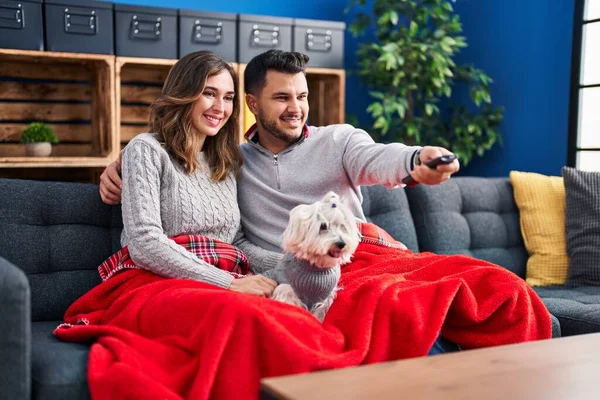 Man and woman watching movie sitting on sofa with dog at home