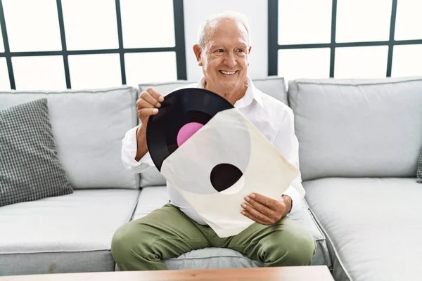 Senior man holding vinyl disc sitting on sofa at home