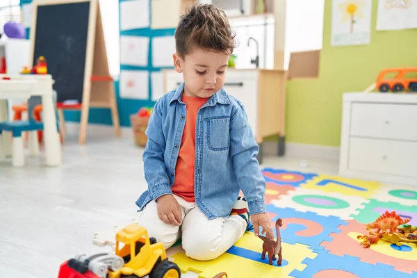 愛らしいヒスパニック幼児遊びとともにトラクターとディノおもちゃ座っています床に幼稚園 — ストック写真