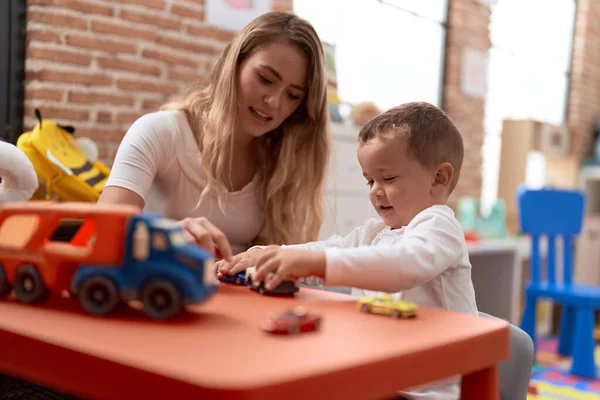 Teacher and toddler playing with cars toy sitting on table at kindergarten