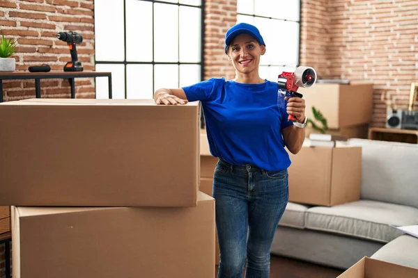 Middle age woman moving worker holding tape packing machine at new home