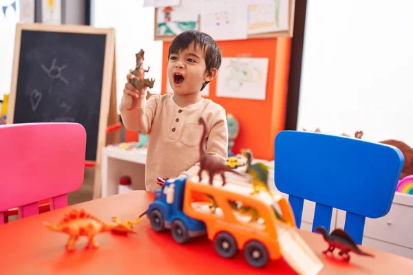 Uroczy Latynoski Chłopiec Bawiący Się Samochodami Zabawkami Dino Stojącymi Przedszkolu — Zdjęcie stockowe