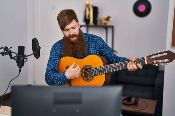 Young redhead man musician playing classical guitar at music studio