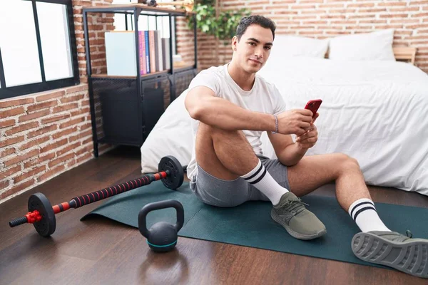 Young Hispanic Man Using Smartphone Sitting Yoga Mat Bedroom — Stockfoto
