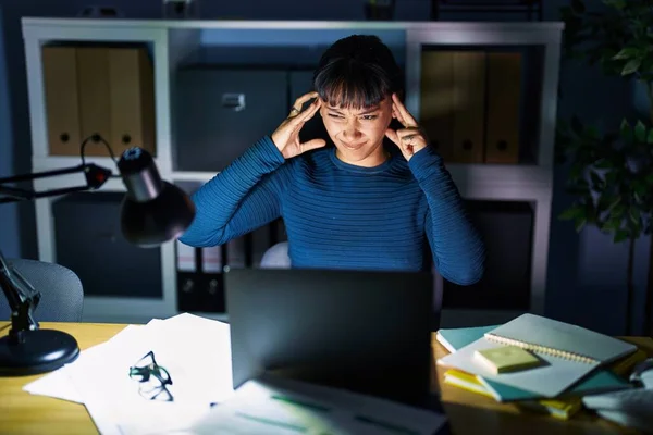 Young beautiful woman working at the office at night covering ears with fingers with annoyed expression for the noise of loud music. deaf concept.