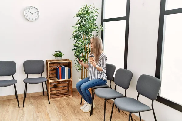 Young chinese woman using smartphone sitting on chair at waiting room