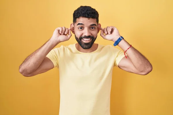 Hispanic Man Beard Standing Yellow Background Smiling Pulling Ears Fingers — Stock fotografie