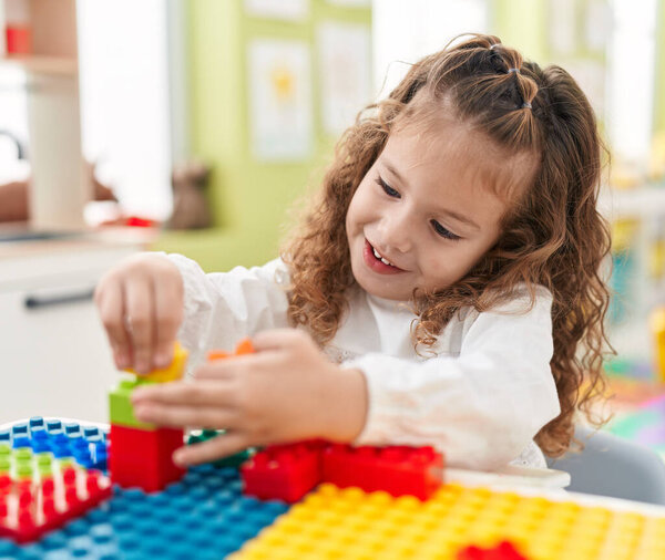 Adorable blonde toddler playing with construction blocks sitting on table at kindergarten