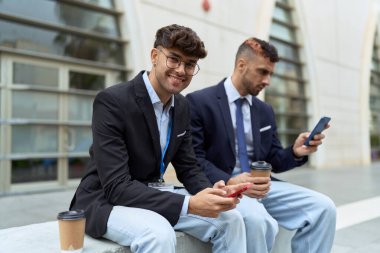 Two hispanic men business workers using smartphones drinking coffee at street