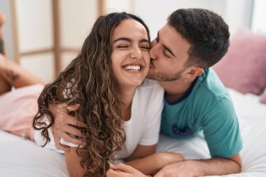 Young hispanic couple lying on bed hugging each other and kissing at bedroom